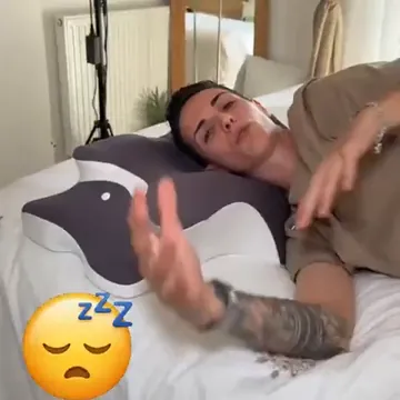 Mujer tumbada en la cama junto a la almohada cervical, mostrándola con la mano